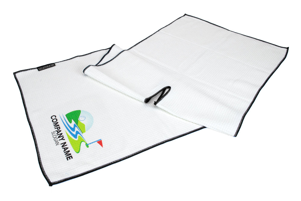 Image shows a folded, center cut microfiber golf towel in white with black trim. An example custom logo design is in the bottom left corner.